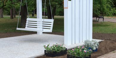 White swing hanging from a pergola in a garden with flower boxes.