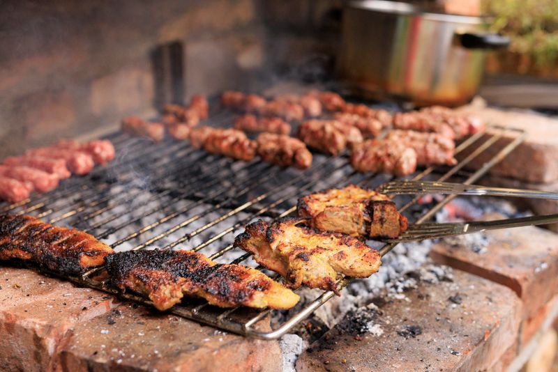 In a backyard setting, various pieces of chicken and vegetables sizzle on a barbecue grill, filling the air with mouthwatering aromas during a summer gathering, pork meat  and traditional Balkan meat rolls  Cevapi, chevapi  grilling  Summer Seasonal Barbecue Foods in Real Settings