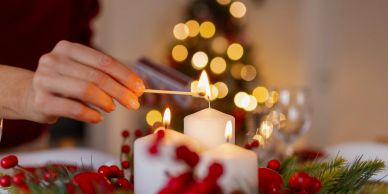 Hand lighting a candle with holiday decorations.