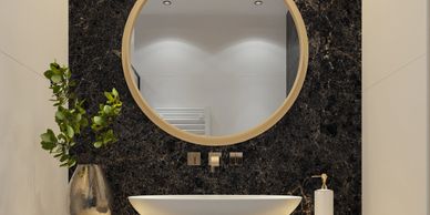 Modern bathroom sink with round mirror and black marble wall.