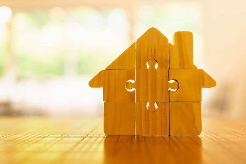Wooden puzzle pieces forming a house symbolizing real estate planning, home building, teamwork, and investment strategy. Great for housing, architecture, finance, or family planning visuals.