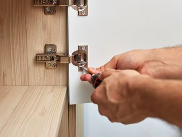 Person tightening a cabinet hinge with a screwdriver.