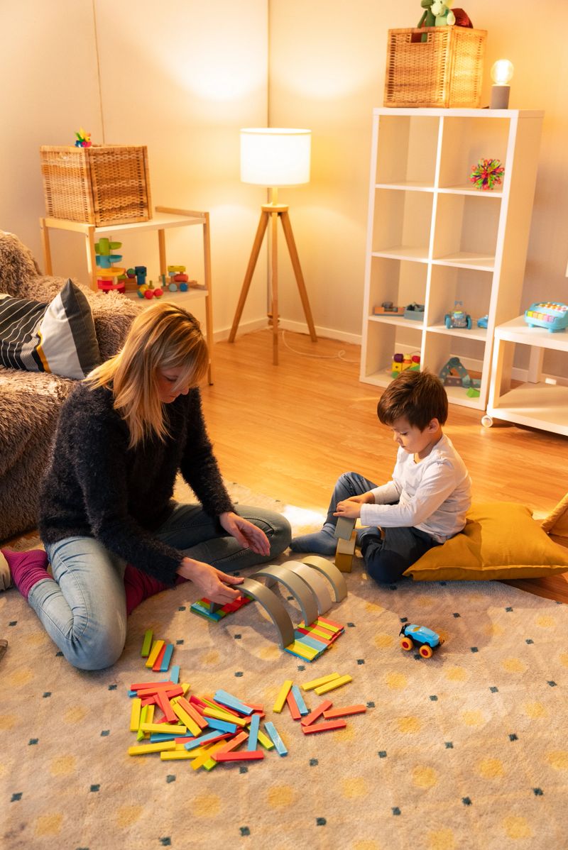 Babysitter and child building with colorful wooden blocks, enjoying playtime together in a cozy playroom