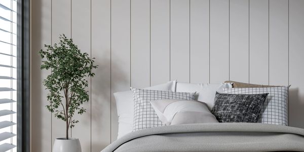 Minimalist bedroom with neutral tones, grid-patterned pillows, and a potted plant near the window.