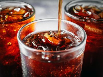 Cold soda being poured into a glass with ice.