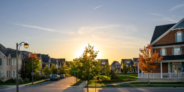 Suburban street at sunset with trees and houses.