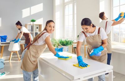 Four people cleaning a bright, modern office space wearing aprons and gloves.