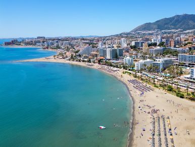 Sunny beach with turquoise water and city skyline.
