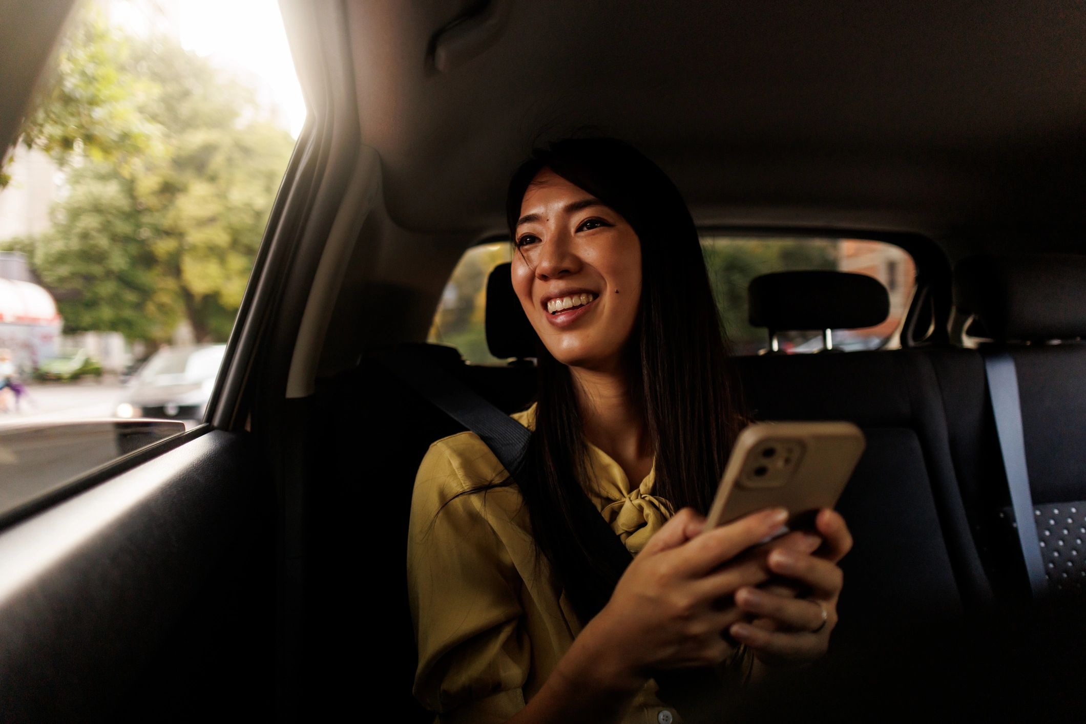 Young woman smiling in the back seat of a car holding a phone.
