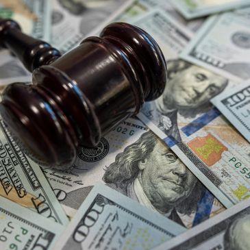 A judge's gavel resting on scattered hundred-dollar bills.