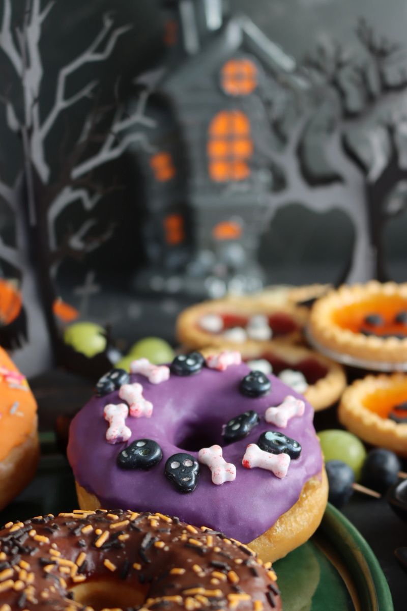 Stock photo shows festive Halloween iced ring doughnuts decorated with colorful candy create a fun and spooky party dessert display. Perfect for themed gatherings, these sweet cakes add playful charm to any celebration
