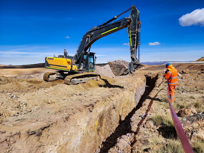 View of an excavator constructing trenches for buried drainage at the edges of an open-pit mine.