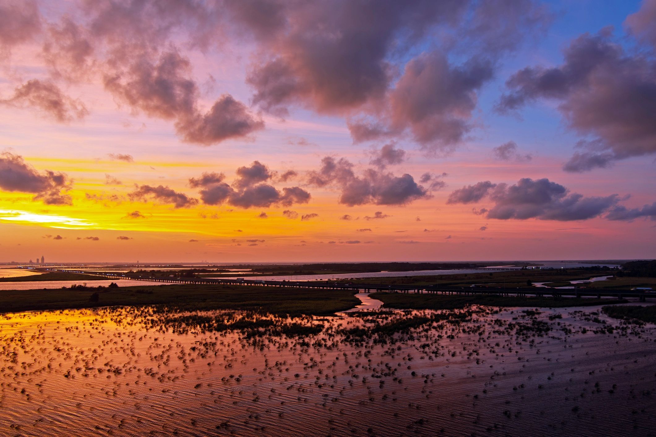 Sunset over a river and wetland with a bridge and clouds.