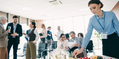 A woman serving snacks at a professional networking event with people mingling in the background.