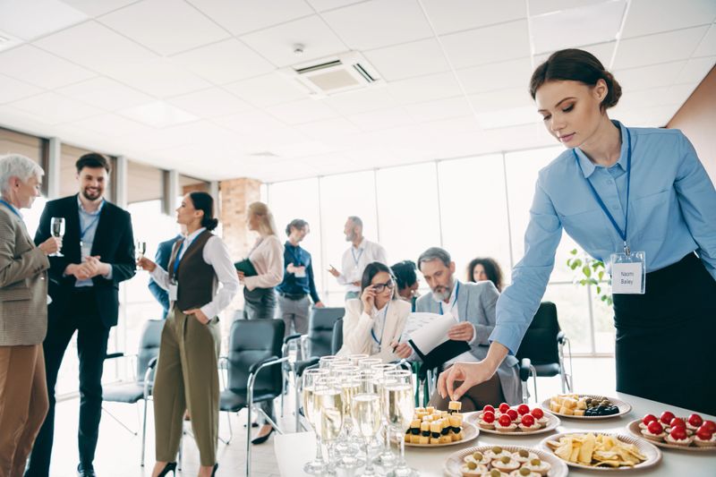 An office scene showing colleagues interacting and collaborating during a business event with refreshments, emphasizing teamwork and corporate atmosphere.