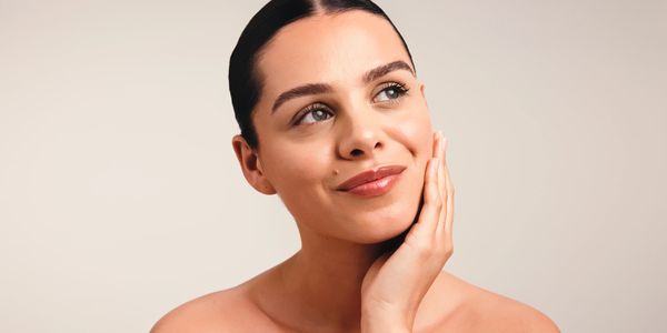 Young woman with clear skin gently touching her face, smiling softly.