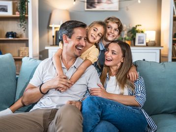 Happy family of four smiling and hugging on a cozy couch at home. comfort, comfortable indoor climate