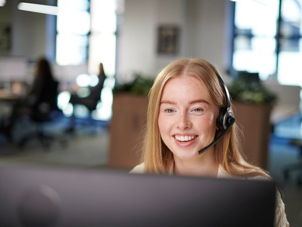 Smiling woman with headset working at computer in office.
