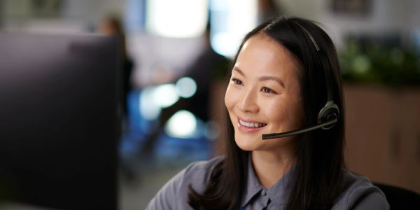 Woman with headset smiling at computer.