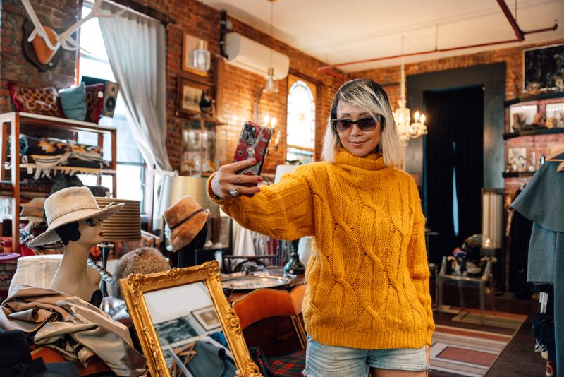 A woman takes a selfie testing sunglasses, surrounded by color and texture.