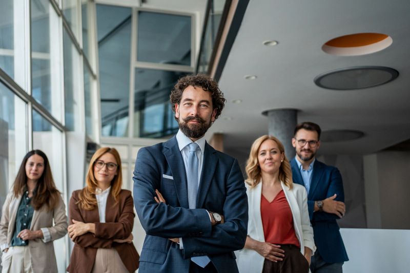 Diverse group of professionals, including both men and women, standing with confidence and looking at the camera, symbolizing teamwork and corporate leadership in a contemporary office setting