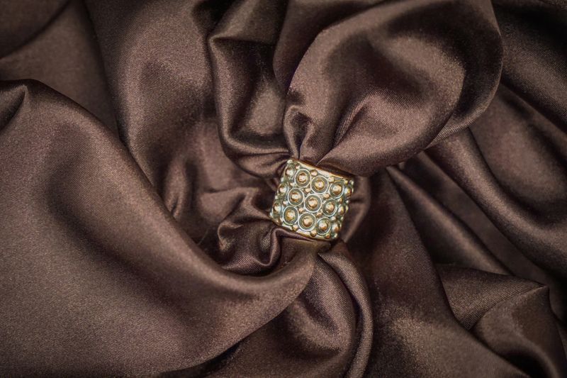 A metallic gold-colored ring on a brown silk background.