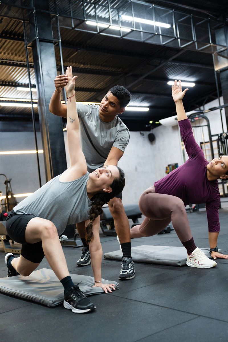 Trainer assisting two women performing a lateral lunge stretch during a fitness class in a modern gym