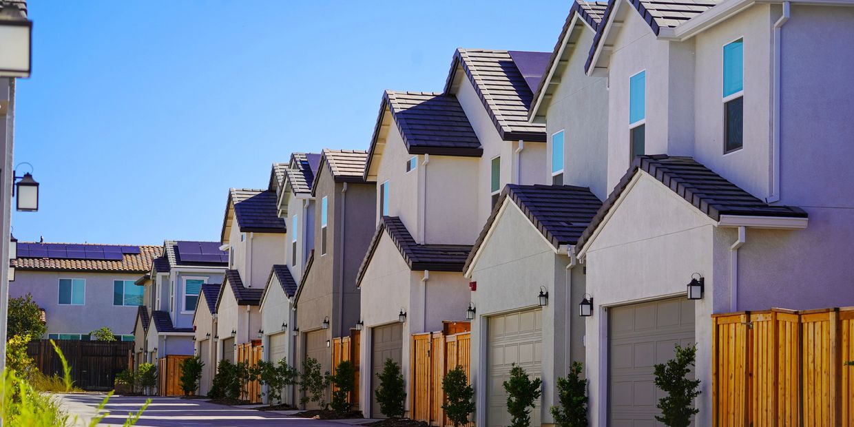 Row of modern suburban houses with garages and wooden fences under clear blue sky.