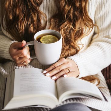 Person holding a mug of lemon tea and reading a book.