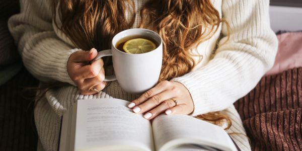 Person holding a cup of tea with lemon while reading a book.