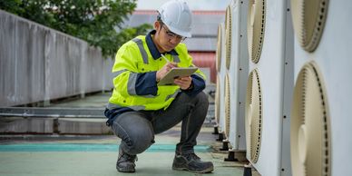 Technician inspecting and recording data near HVAC units on a rooftop.