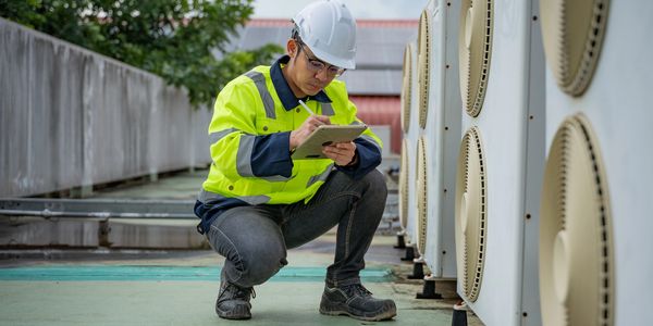 Technician inspecting and recording data near HVAC units on a rooftop.