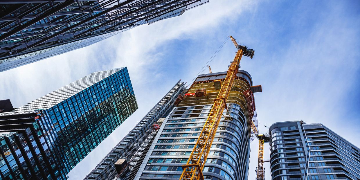 Skyscrapers and construction cranes under a blue sky.