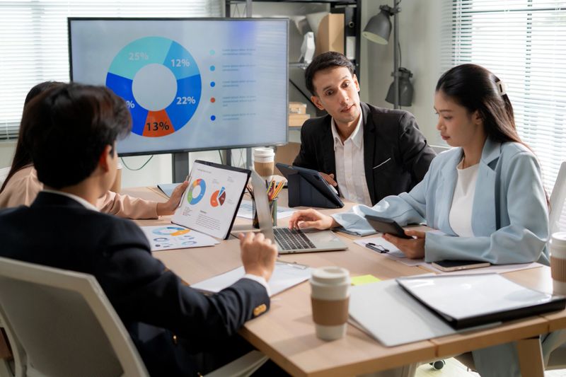 Group business team meeting with businessman explaining strategy report marketing in office, colleague analyzing chart data on display screen and planning growth financial and investment of business.
