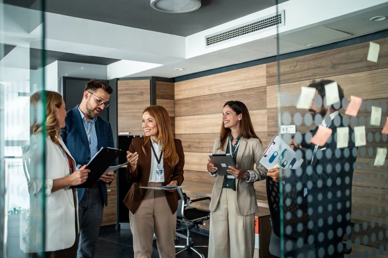 Diverse business colleagues brainstorming and strategizing in a modern office, standing and collaborating energetically to plan projects, communicate ideas and drive team success