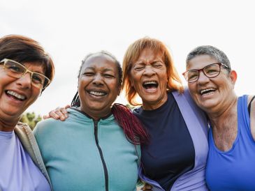 Four joyful older women smiling and embracing outdoors.