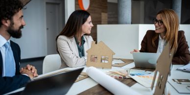 Three professionals discussing a house model in an office.