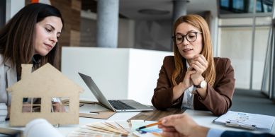 Two women discussing house plans at a table.