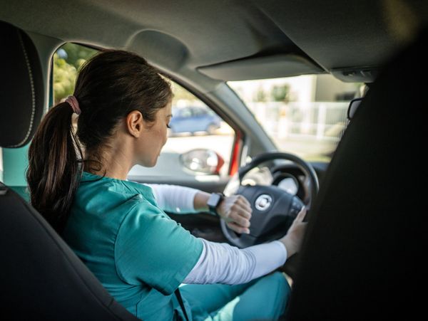 A nurse in scrubs checks her smartwatch while sitting in a car.