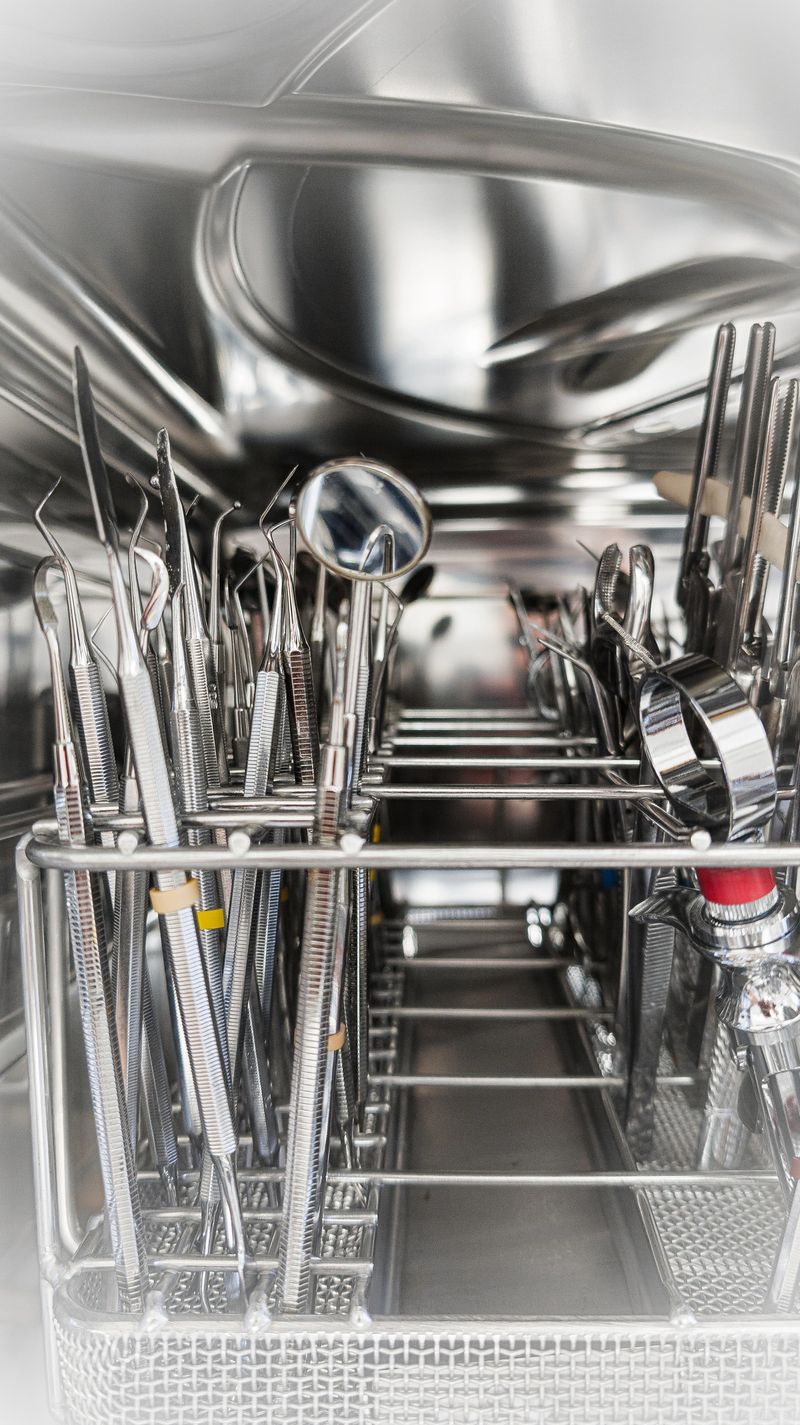 Bright macro photo of multiple stainless steel dental instruments placed neatly in a metal holder inside a thermal disinfector. Every tool is in focus, reflecting light and emphasizing professional hygiene, order, and cleanliness in modern dentistry. Perfect representation of sterile dental workflow and instrument care.