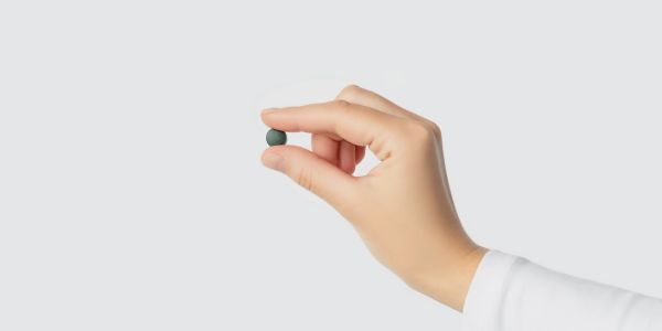 Hand holding a small green pill.