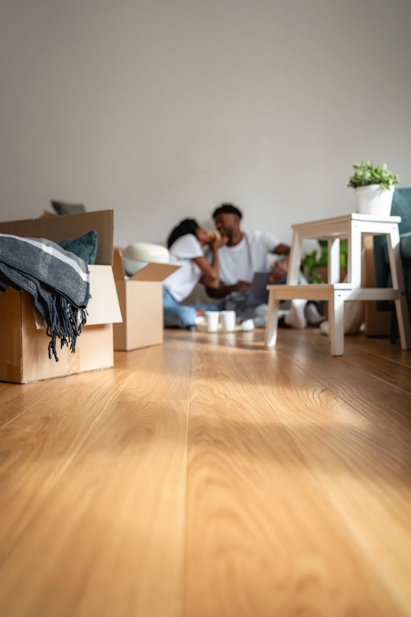 Smiling African American couple sitting on the floor among moving boxes, using a laptop together. Happy moment of love, teamwork, and excitement while planning their new home life