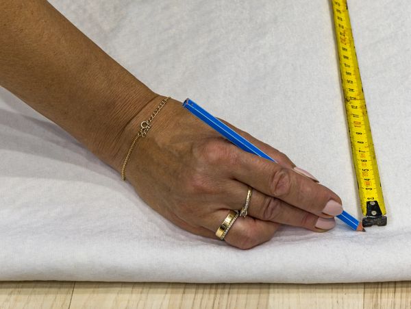 Hand marking fabric with pencil using a tape measure for precise cutting.