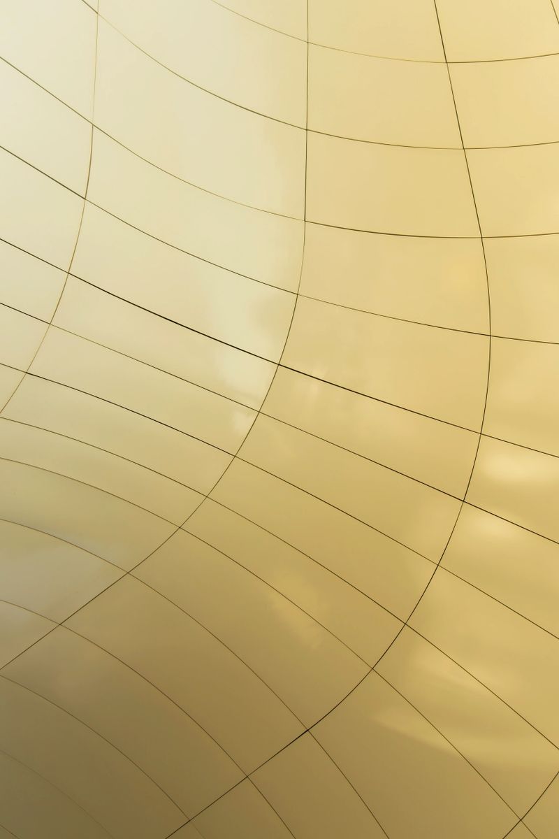 A close-up of glossy golden panels forming a curved grid. Light and shadows create a sense of calm luxury, modern design, and abstract architectural beauty.