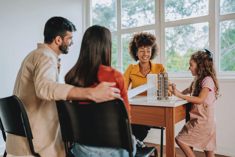 A real estate agent talking with a family and their young daughter during a property meeting in a bright apartment, discussing new home options and real estate investment. Concept of family housing, buying or renting property, and new beginnings
