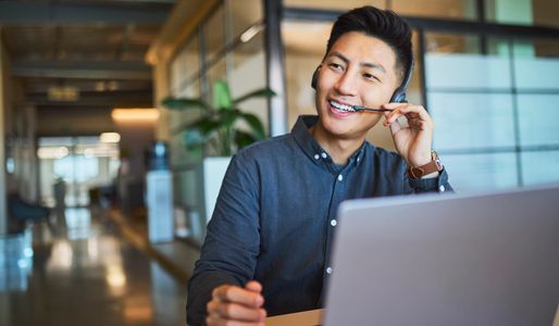 Man smiling while wearing a headset and working on a laptop.