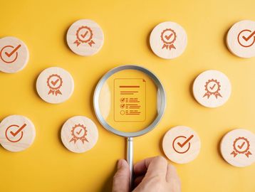 Magnifying glass highlighting a checklist among wooden tokens with checkmark and badge icons.