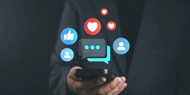 Hand holding phone with social media icons floating above.