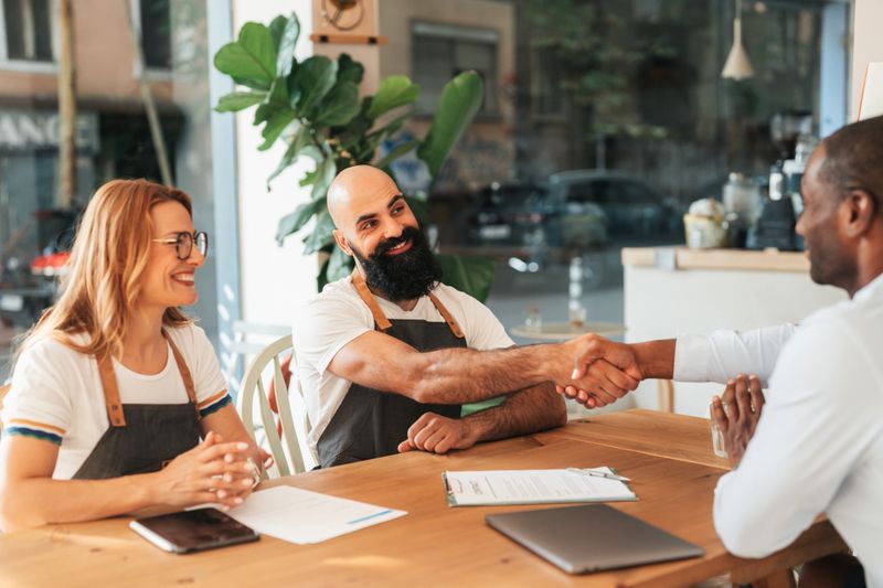 Cafe owners shaking hands with a financial consultant during a business meeting. Concept of small business financing, entrepreneurship, investment, and support for local businesses.