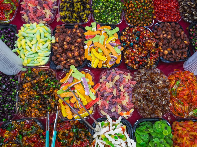 A vibrant overhead display of an assortment of colorful gummy candies and dried fruits in bulk bins, showcasing a tempting variety of sweets and treats. Perfect for confectionery themes.